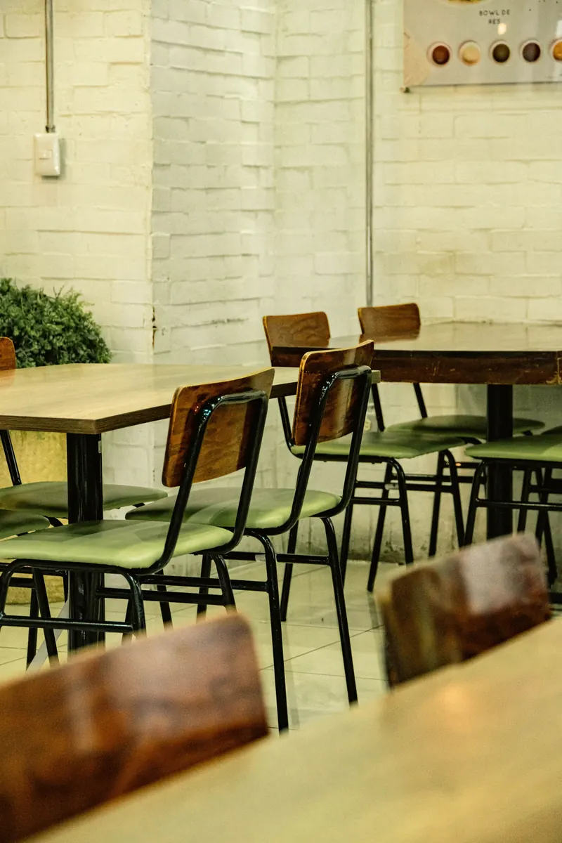 La sala, con sillas verdes y mesas de madera